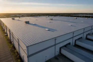 A finished standing seam metal roof on a large distribution center with loading docks visible below.